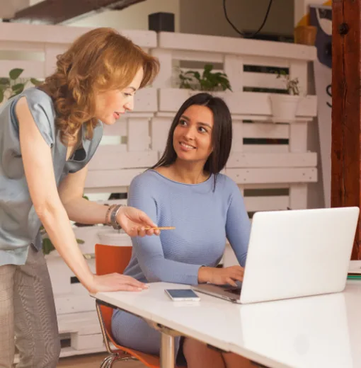 Two women collaborating at a laptop in a bright office